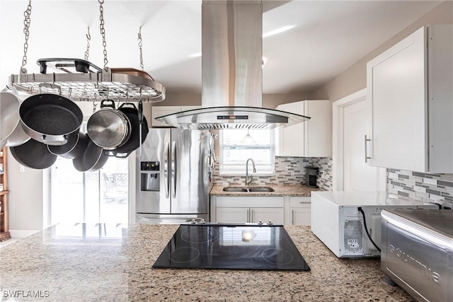 kitchen with sink, stainless steel fridge, white cabinetry, black electric stovetop, and island exhaust hood