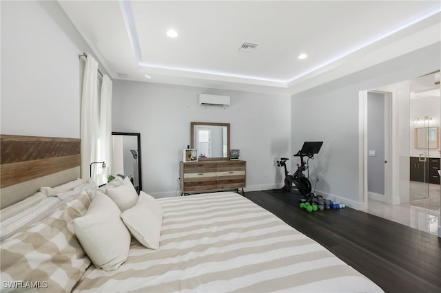 bedroom featuring dark wood-type flooring, a tray ceiling, and a wall unit AC