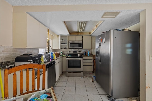 kitchen featuring light tile patterned floors, stainless steel appliances, tasteful backsplash, a textured ceiling, and white cabinets