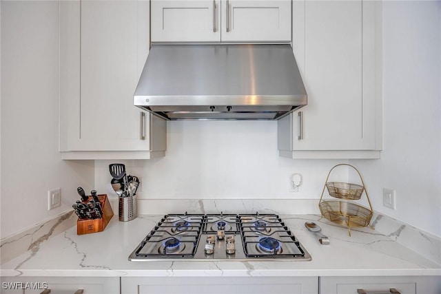 kitchen with light stone counters, white cabinets, range hood, and stainless steel gas stovetop