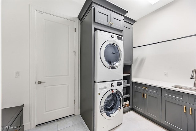 clothes washing area with cabinets, stacked washing maching and dryer, sink, and light tile patterned floors