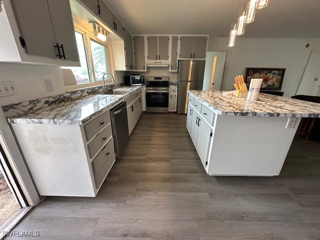 kitchen with sink, hanging light fixtures, stainless steel appliances, a center island, and light stone counters