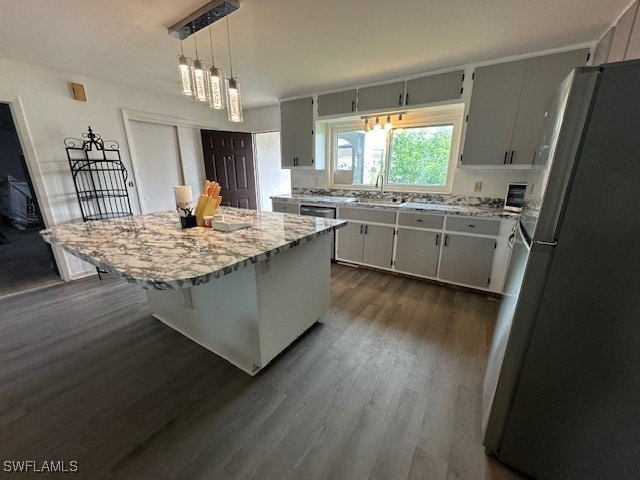 kitchen featuring a kitchen island, stainless steel refrigerator, decorative light fixtures, sink, and dark hardwood / wood-style flooring