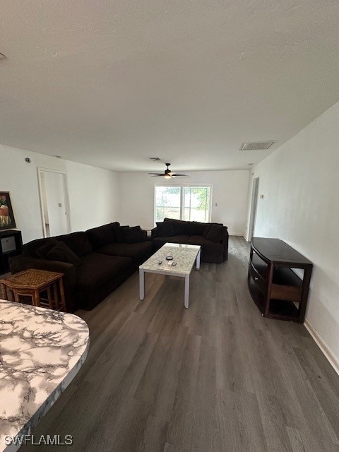 living room featuring ceiling fan, dark wood-type flooring, and a textured ceiling