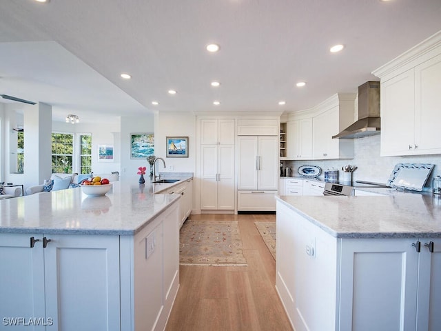 kitchen featuring sink, white cabinets, paneled built in refrigerator, light stone counters, and wall chimney exhaust hood