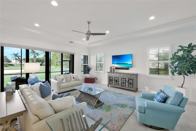 tiled living room with ceiling fan, plenty of natural light, a raised ceiling, and ornamental molding