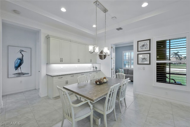 tiled dining space with a raised ceiling, ornamental molding, and a chandelier