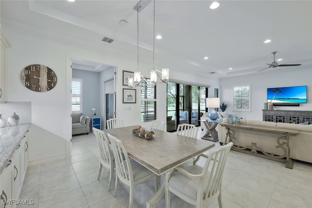 tiled dining area featuring crown molding, a tray ceiling, ceiling fan with notable chandelier, and a healthy amount of sunlight