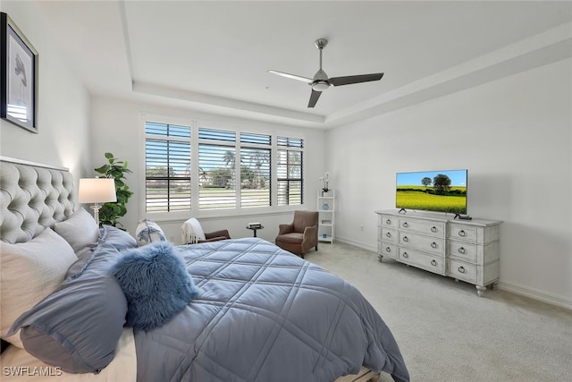 carpeted bedroom with ceiling fan and a tray ceiling