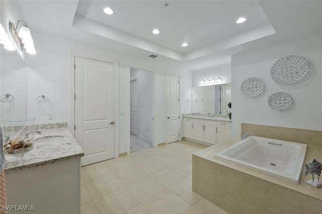 bathroom with vanity, tiled tub, a tray ceiling, and tile patterned floors