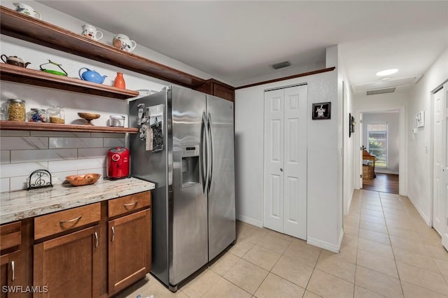 kitchen with stainless steel refrigerator with ice dispenser, light tile patterned flooring, light stone counters, and decorative backsplash