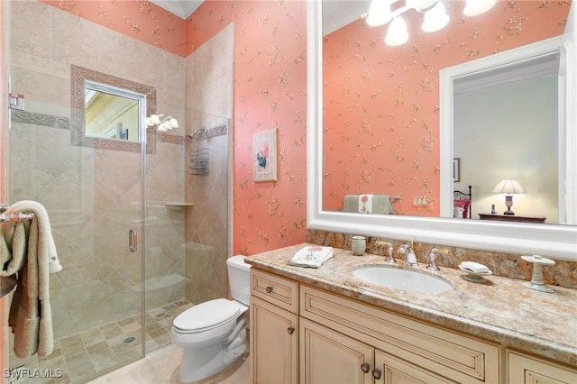 bathroom with vanity, a shower stall, toilet, and wallpapered walls