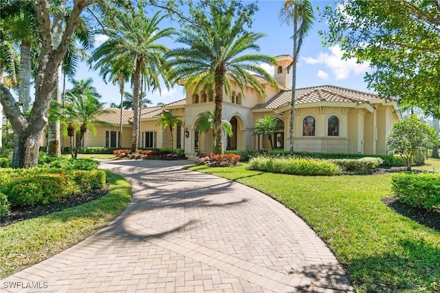 mediterranean / spanish house featuring decorative driveway, a tiled roof, a front lawn, and stucco siding