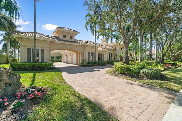 mediterranean / spanish home featuring a tiled roof, a front lawn, decorative driveway, and stucco siding