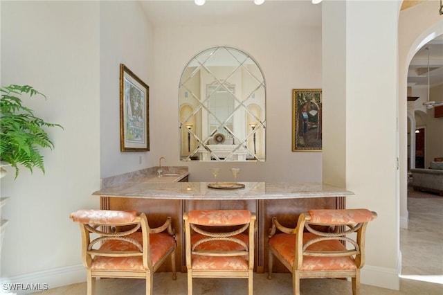 bar with arched walkways, baseboards, a sink, and wet bar