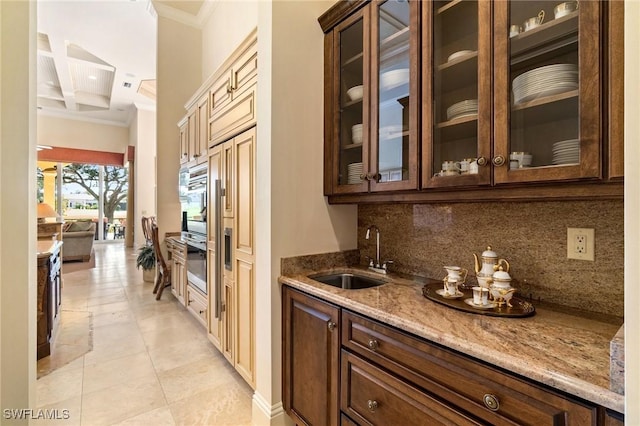 bar with sink, light stone counters, ornamental molding, oven, and decorative backsplash