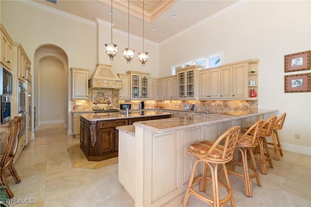 kitchen featuring a kitchen bar, hanging light fixtures, light stone counters, kitchen peninsula, and crown molding