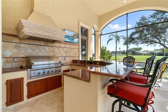 kitchen with dark stone counters, decorative backsplash, custom range hood, a kitchen breakfast bar, and a peninsula