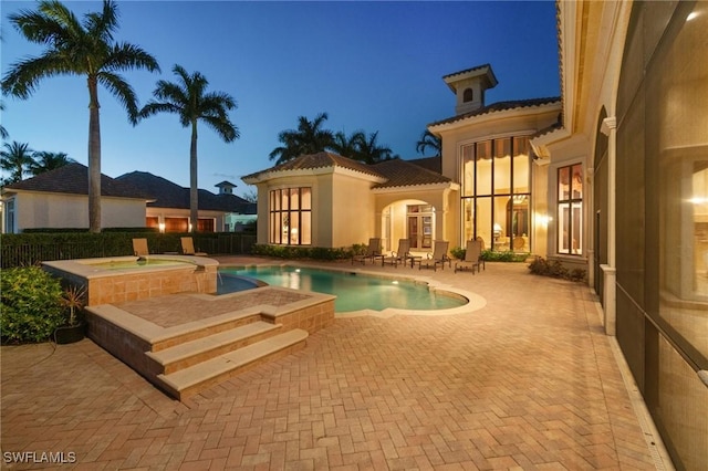 pool at dusk featuring an in ground hot tub and a patio