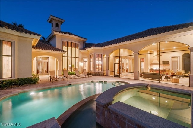 pool at night with a pool with connected hot tub, french doors, and a patio