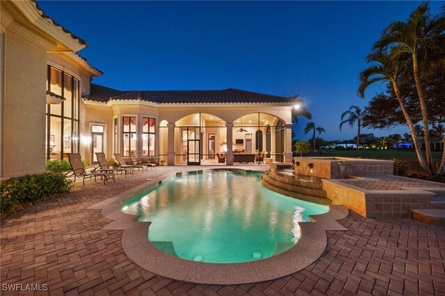 pool at night with ceiling fan and a patio