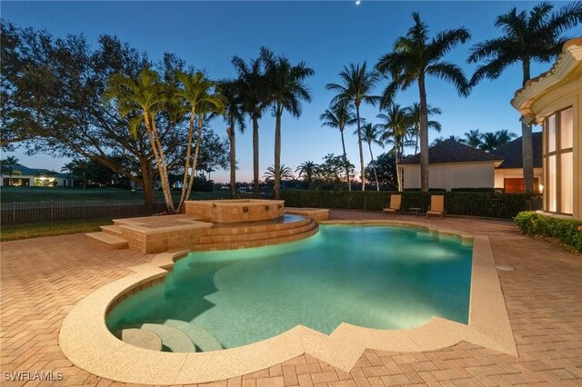 pool at dusk featuring a hot tub and a patio