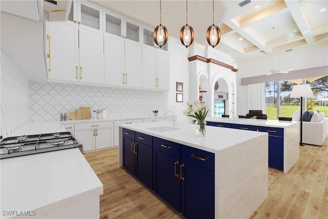 kitchen with sink, white cabinetry, hanging light fixtures, light wood-type flooring, and an island with sink