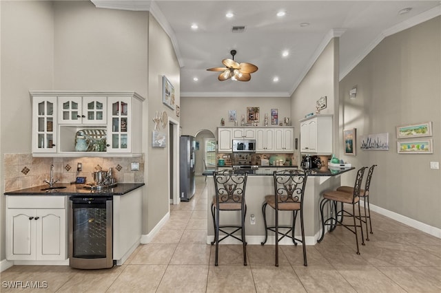 kitchen with crown molding, tasteful backsplash, stainless steel appliances, beverage cooler, and white cabinets