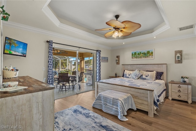 bedroom featuring crown molding, wood-type flooring, a tray ceiling, and access to exterior