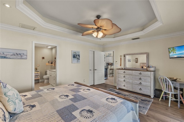 bedroom with a tray ceiling, ornamental molding, light hardwood / wood-style floors, and ensuite bath