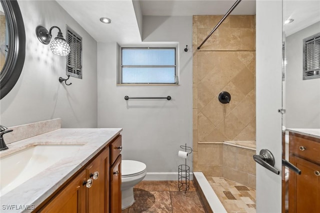 bathroom with a tile shower, vanity, and toilet