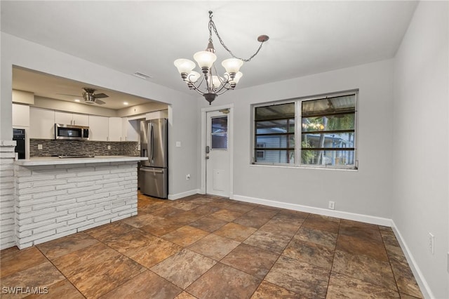 kitchen with appliances with stainless steel finishes, ceiling fan with notable chandelier, decorative light fixtures, tasteful backsplash, and white cabinets