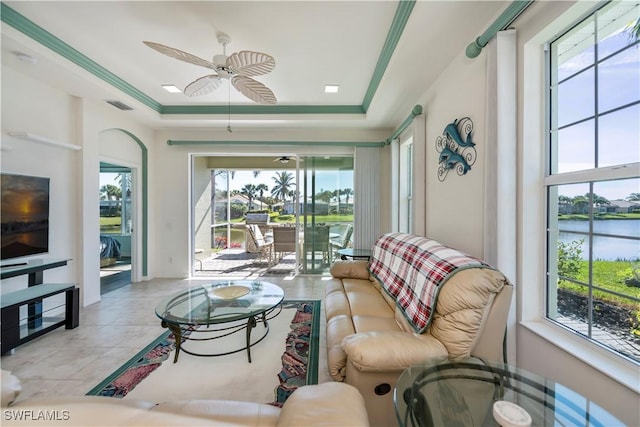 living room featuring a tray ceiling, light tile patterned flooring, ceiling fan, and a water view