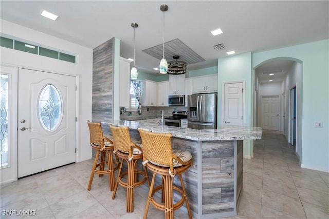 kitchen with white cabinetry, appliances with stainless steel finishes, a kitchen breakfast bar, pendant lighting, and light stone countertops