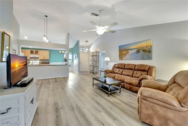 living room featuring ceiling fan with notable chandelier, high vaulted ceiling, and light wood-type flooring