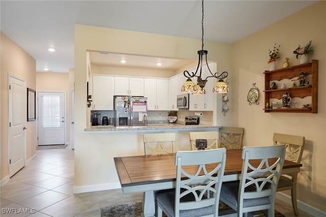 kitchen featuring white cabinets, hanging light fixtures, kitchen peninsula, stainless steel appliances, and light stone countertops