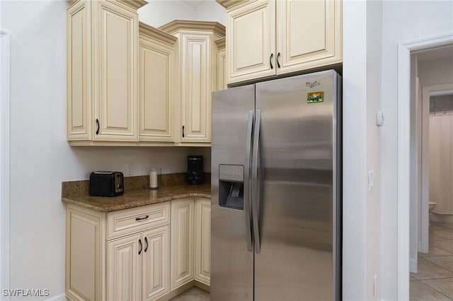 kitchen with stainless steel refrigerator with ice dispenser, dark stone countertops, light tile patterned floors, and cream cabinetry