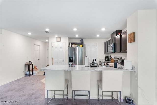 kitchen featuring stainless steel appliances, light colored carpet, a kitchen breakfast bar, and kitchen peninsula