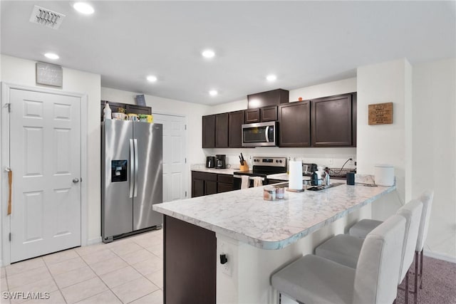 kitchen with light tile patterned flooring, appliances with stainless steel finishes, a breakfast bar area, kitchen peninsula, and dark brown cabinets