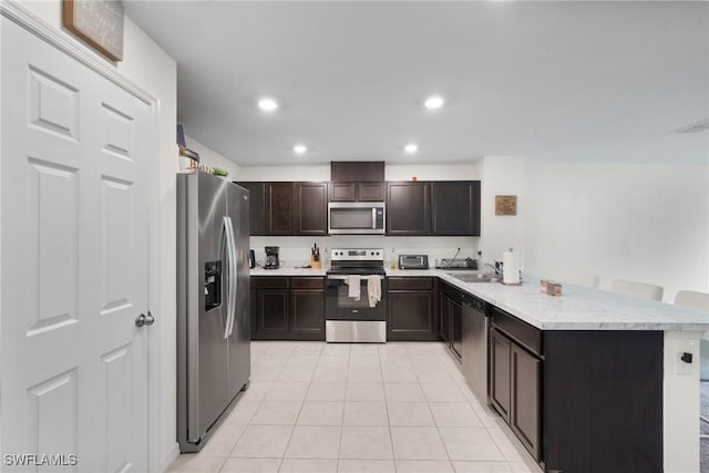 kitchen featuring sink, dark brown cabinets, appliances with stainless steel finishes, a kitchen breakfast bar, and kitchen peninsula