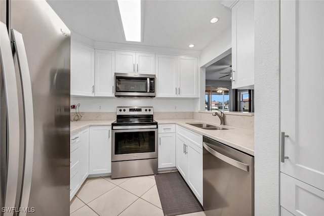 kitchen with sink, light tile patterned floors, ceiling fan, appliances with stainless steel finishes, and white cabinets