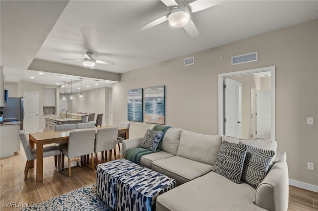 living room featuring sink, ceiling fan, and light wood-type flooring