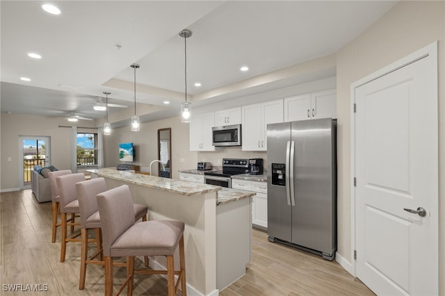 kitchen featuring stainless steel appliances, light stone countertops, a kitchen island with sink, and white cabinets