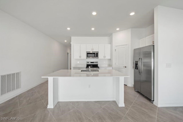 kitchen with light tile patterned flooring, appliances with stainless steel finishes, white cabinetry, sink, and a center island with sink