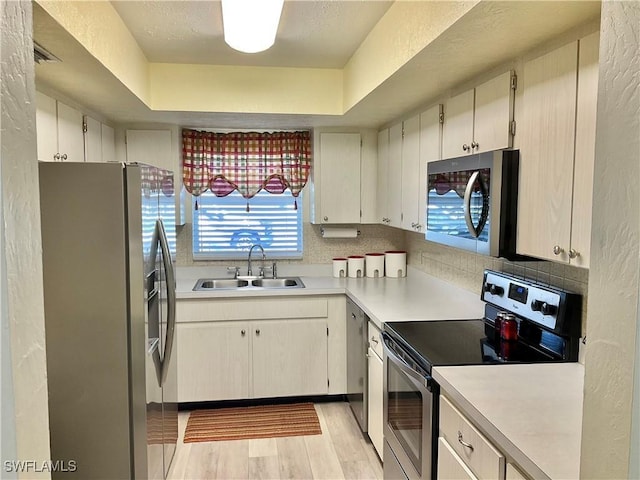 kitchen featuring sink, stainless steel appliances, tasteful backsplash, a tray ceiling, and light hardwood / wood-style floors