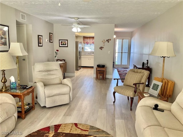 living room with sink, light hardwood / wood-style floors, a textured ceiling, and ceiling fan