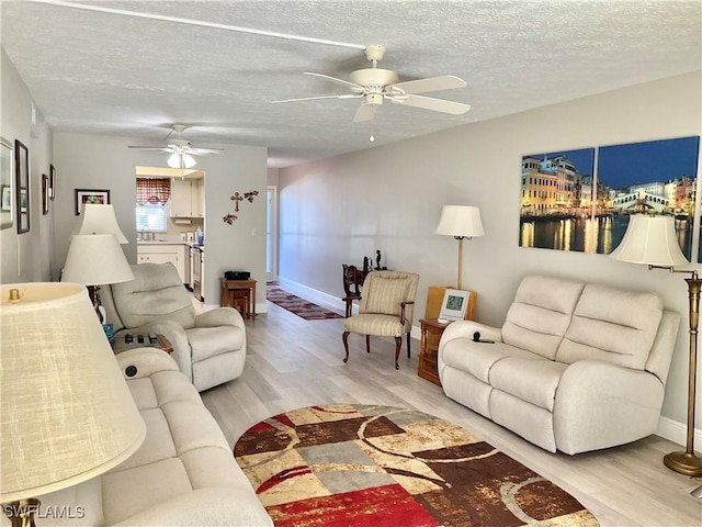 living room with ceiling fan, a textured ceiling, and light hardwood / wood-style flooring