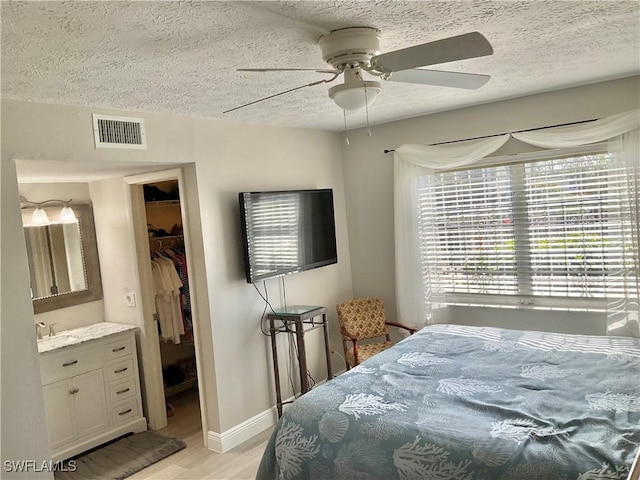 bedroom with light wood-type flooring, a walk in closet, ceiling fan, a textured ceiling, and a closet