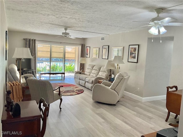 living room featuring ceiling fan, light hardwood / wood-style floors, and a textured ceiling