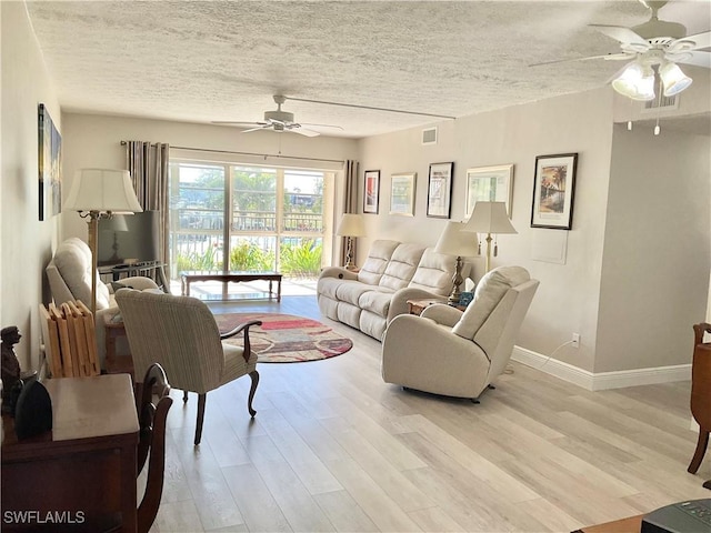 living room featuring ceiling fan, light hardwood / wood-style flooring, and a textured ceiling